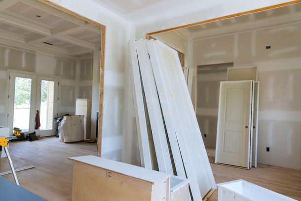 Unfinished room with drywall, leaning white panels, and doors in a bright interior under renovation