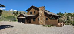 Rustic stone-and-wood cabin with a chimney on a gravel lot under a clear blue sky
