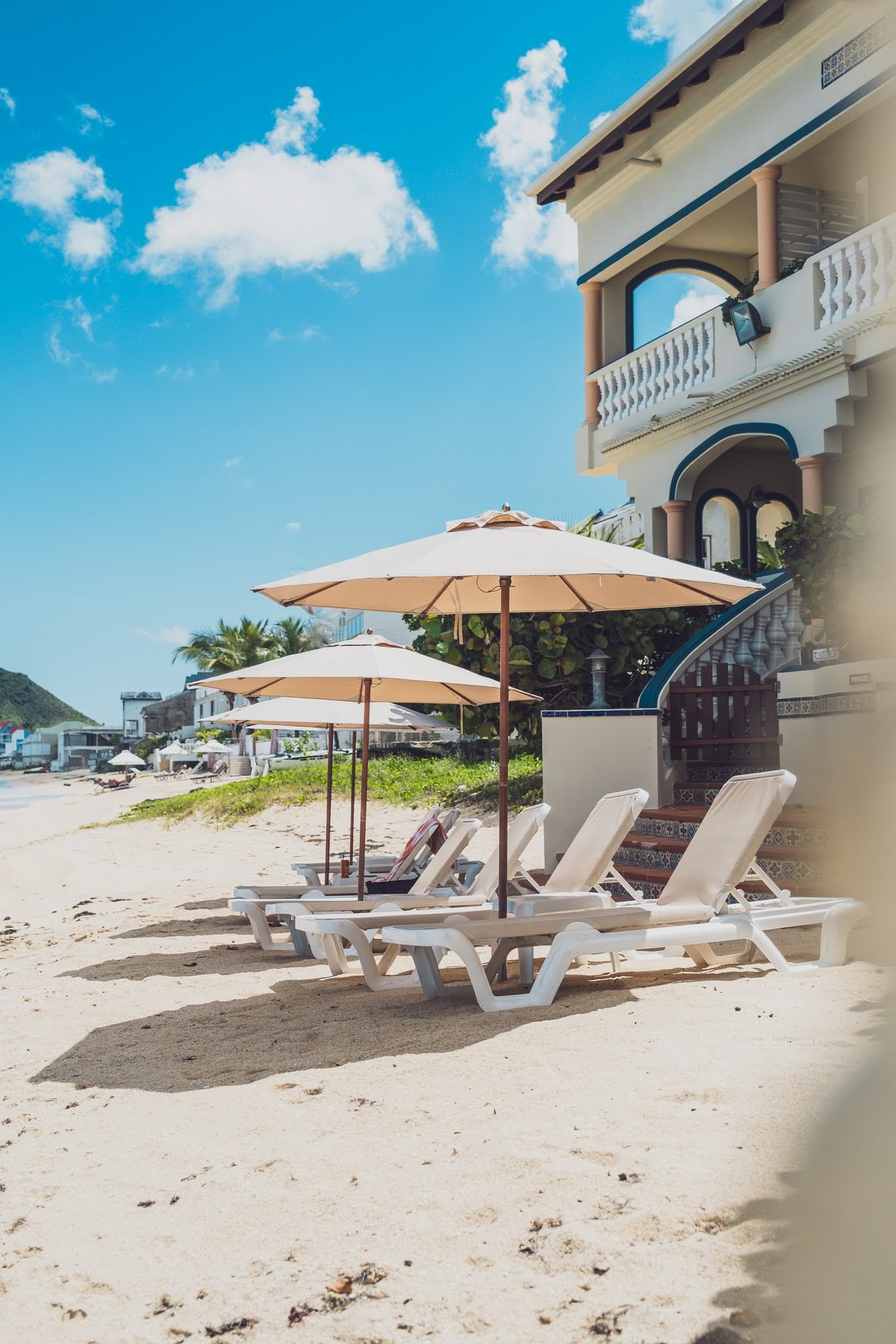 Beach scene with lounge chairs, umbrellas, and building under a blue sky.