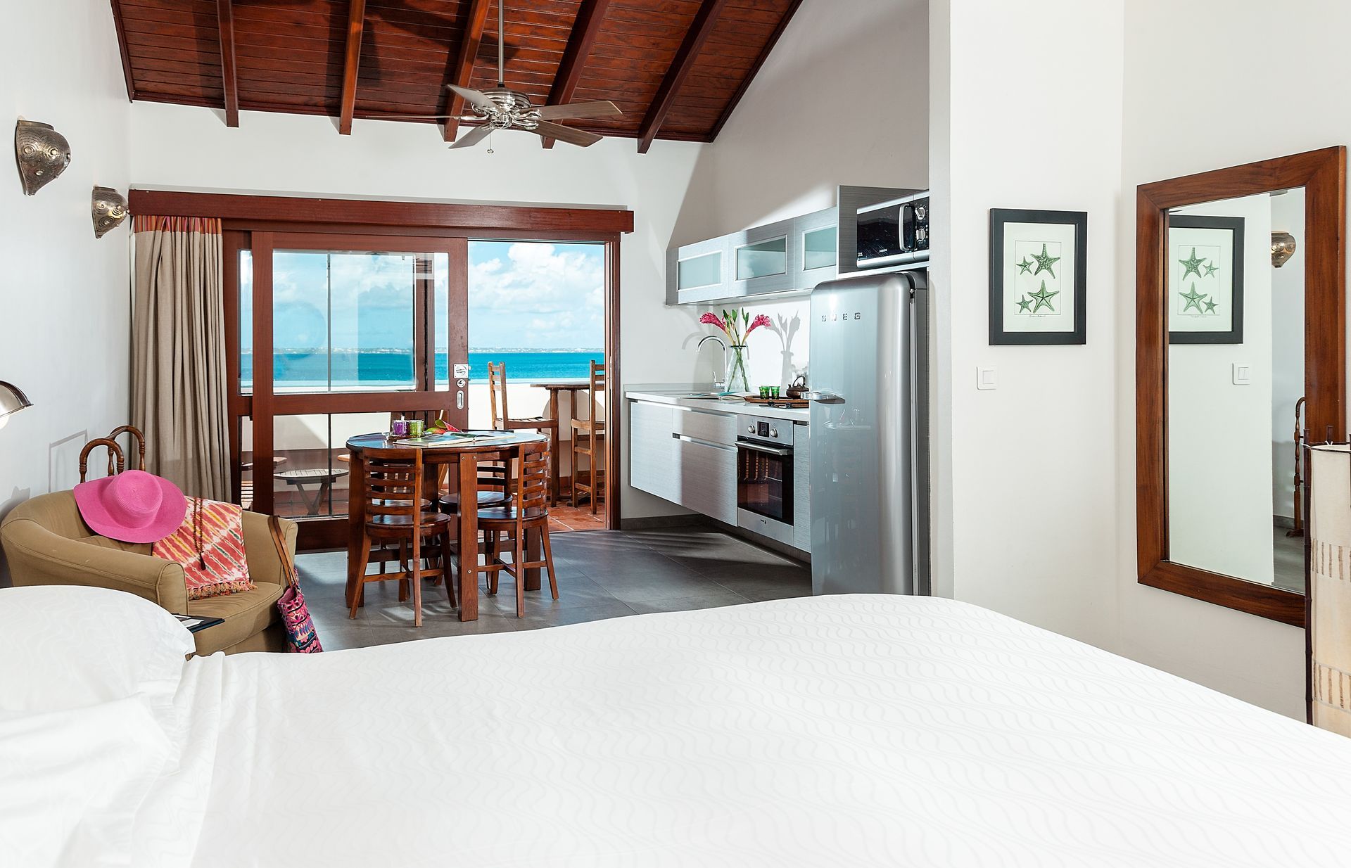 Beachfront studio apartment interior with ocean view, kitchen, bed, and dining area.