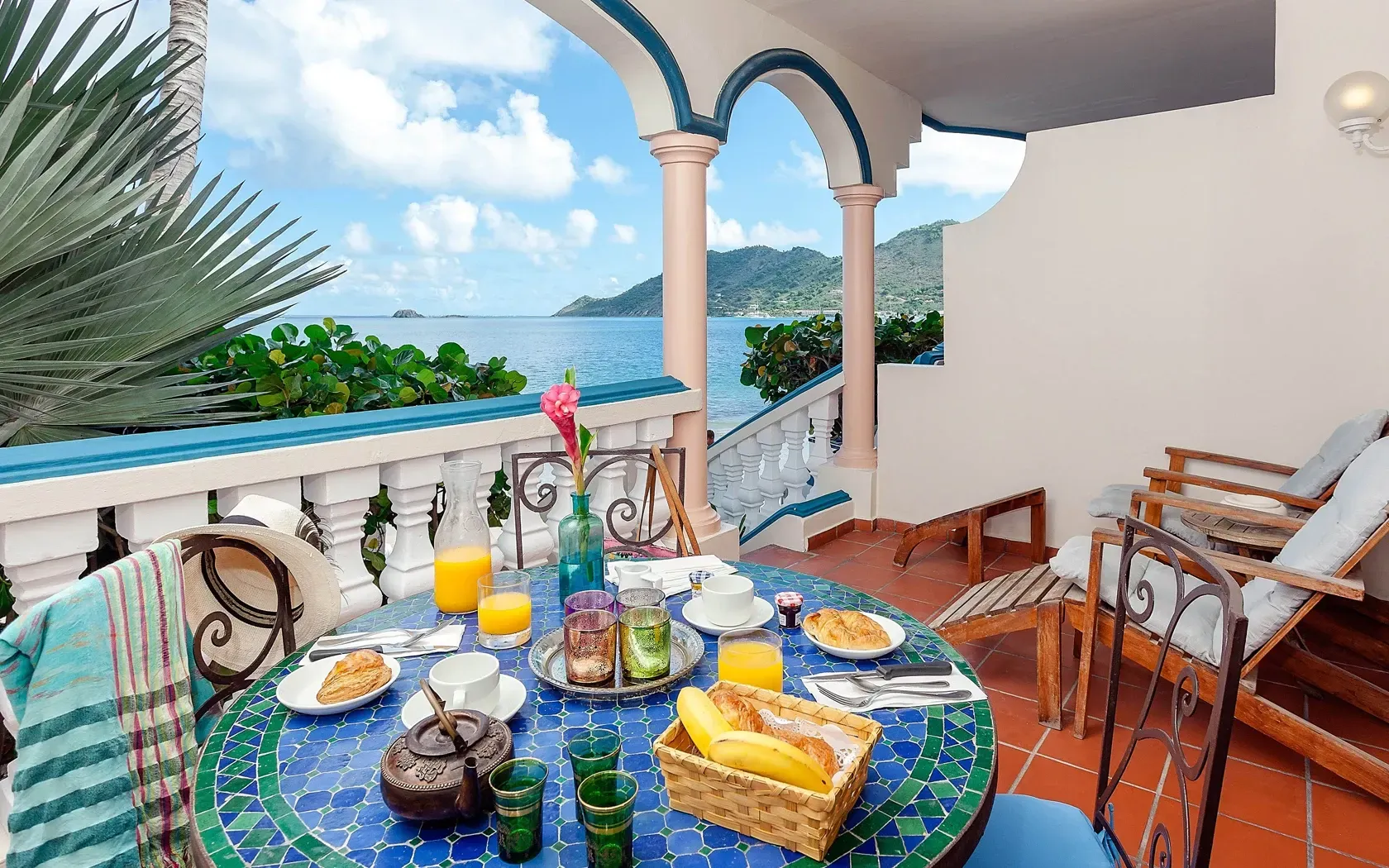 Breakfast table on balcony overlooking ocean. Blue mosaic table, fruit, juice, sunny day.
