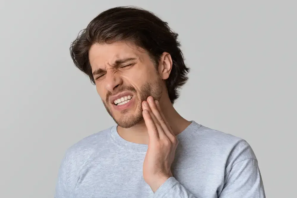 Man grimaces, holding his jaw, showing signs of tooth pain.