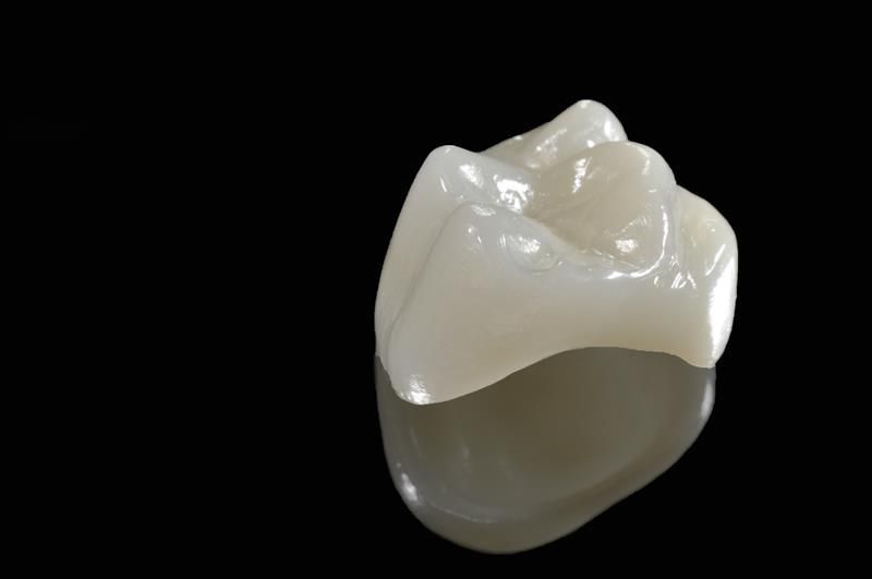 Dental crown on a reflective black surface, appearing white with natural tooth structure details.