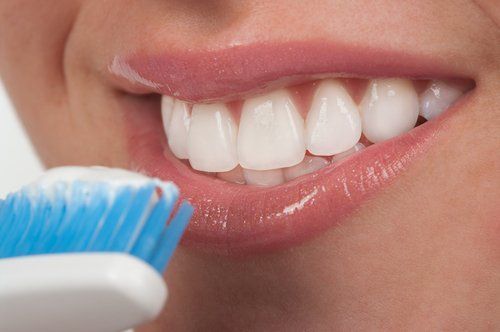 Close-up of a person's mouth with white teeth; a toothbrush with blue bristles and white toothpaste is next to them.