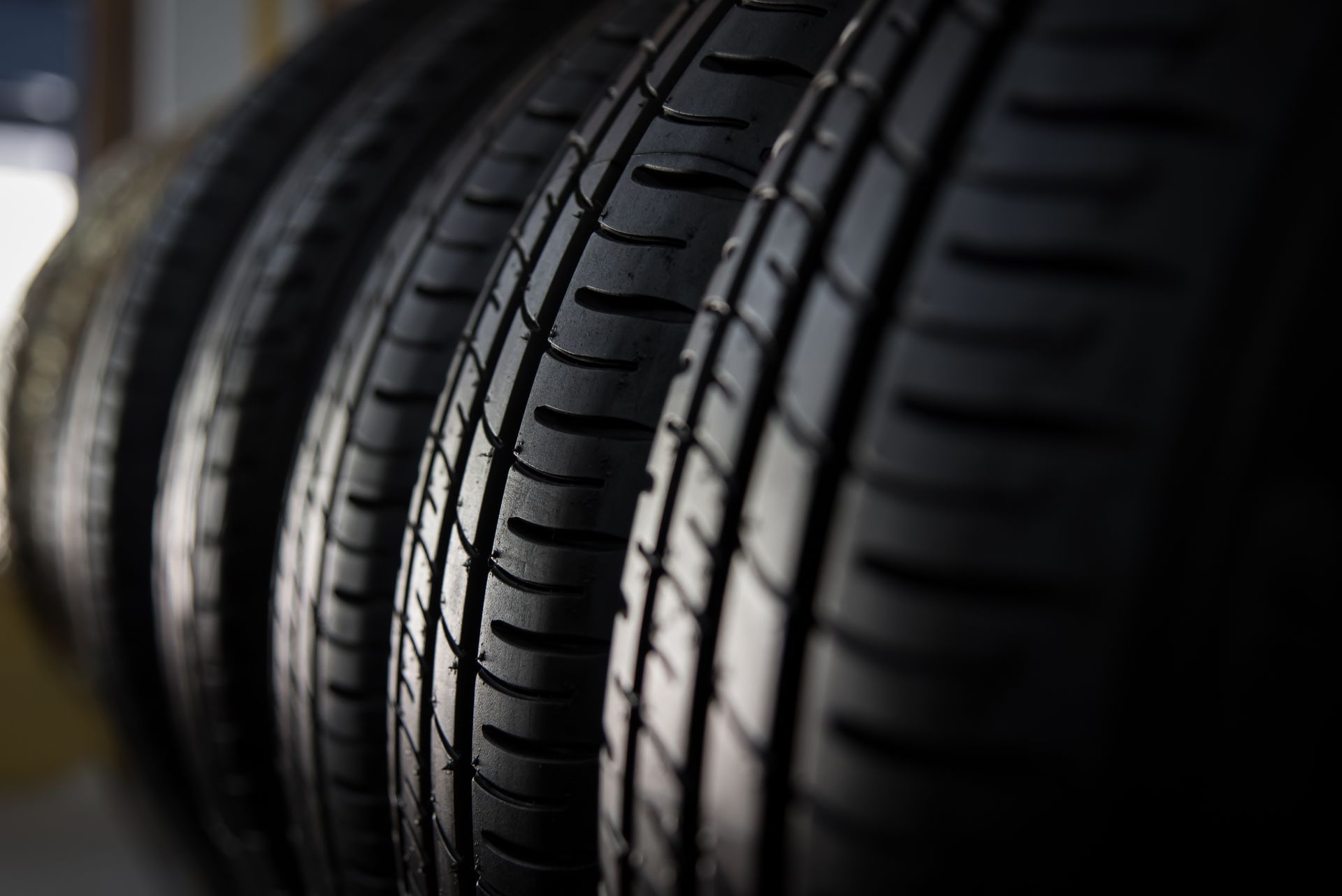 Close-up of stacked black car tires with deep tread patterns in a dimly lit setting