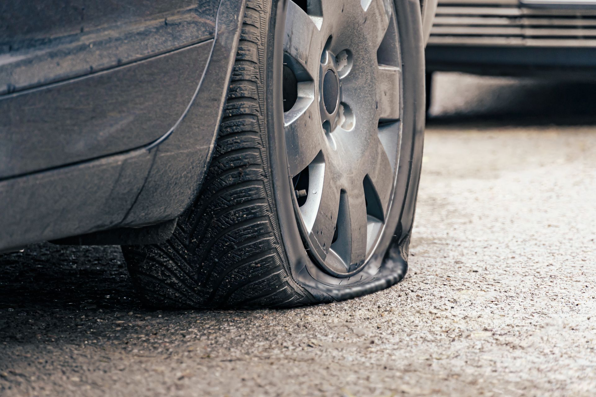 Flat tire on a silver car parked on a wet road.