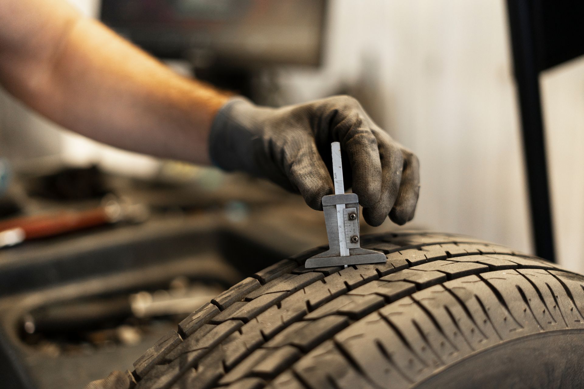 Gloved hand using a tire tread depth gauge on a car tire in a workshop