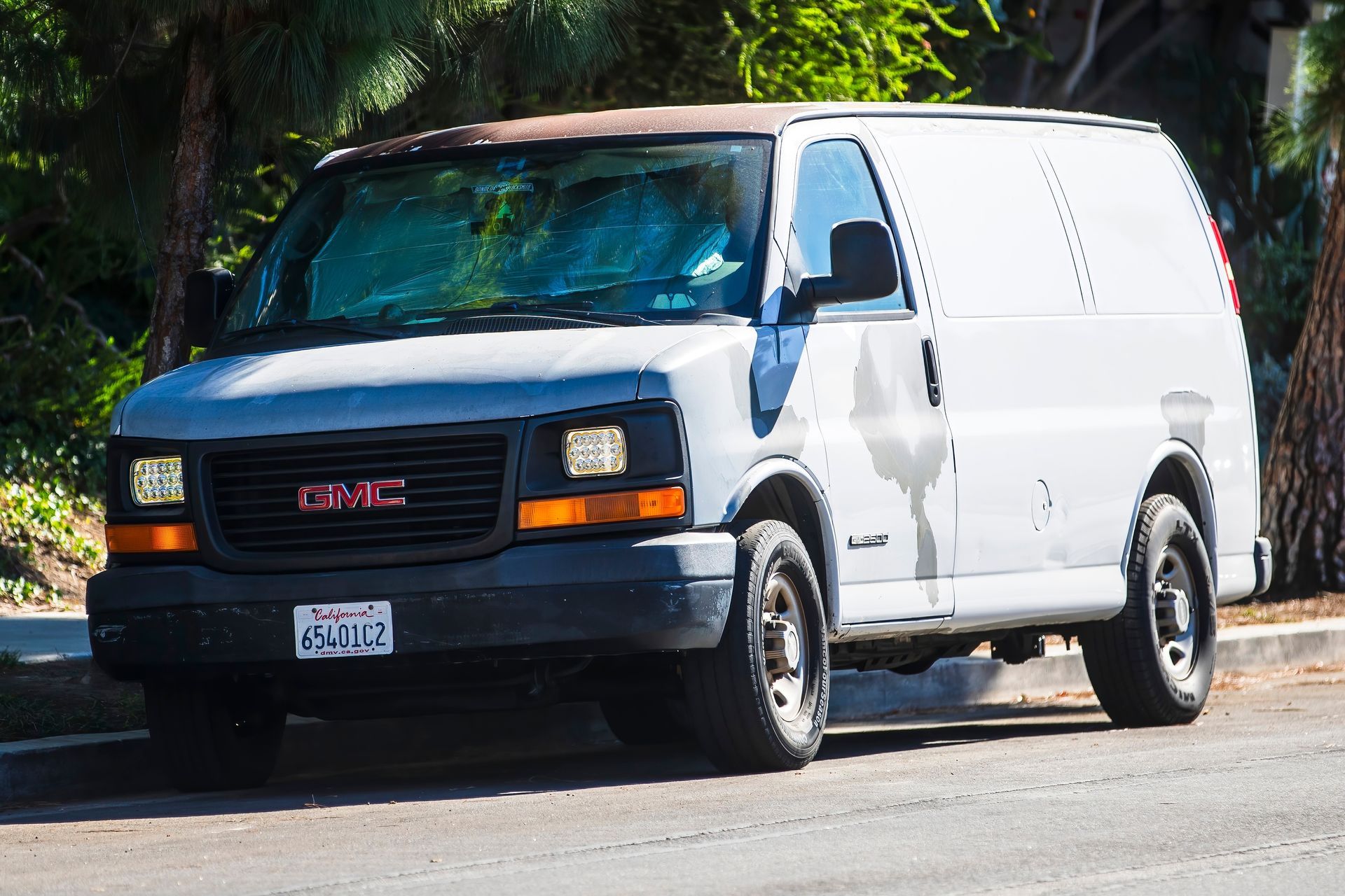 White cargo van driving on a sunny street with palm trees nearby