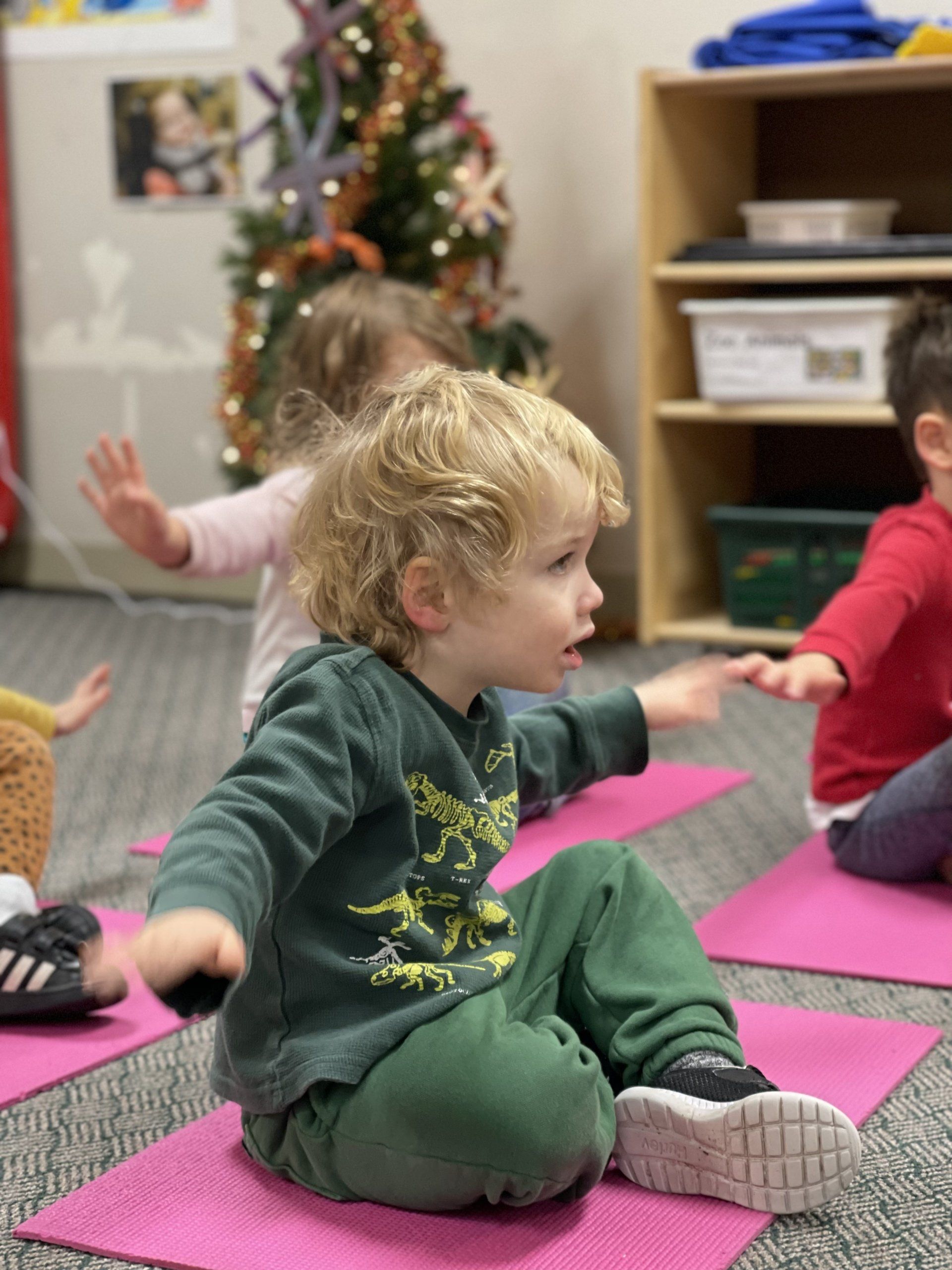 Young children on pink mats doing stretches in a classroom.