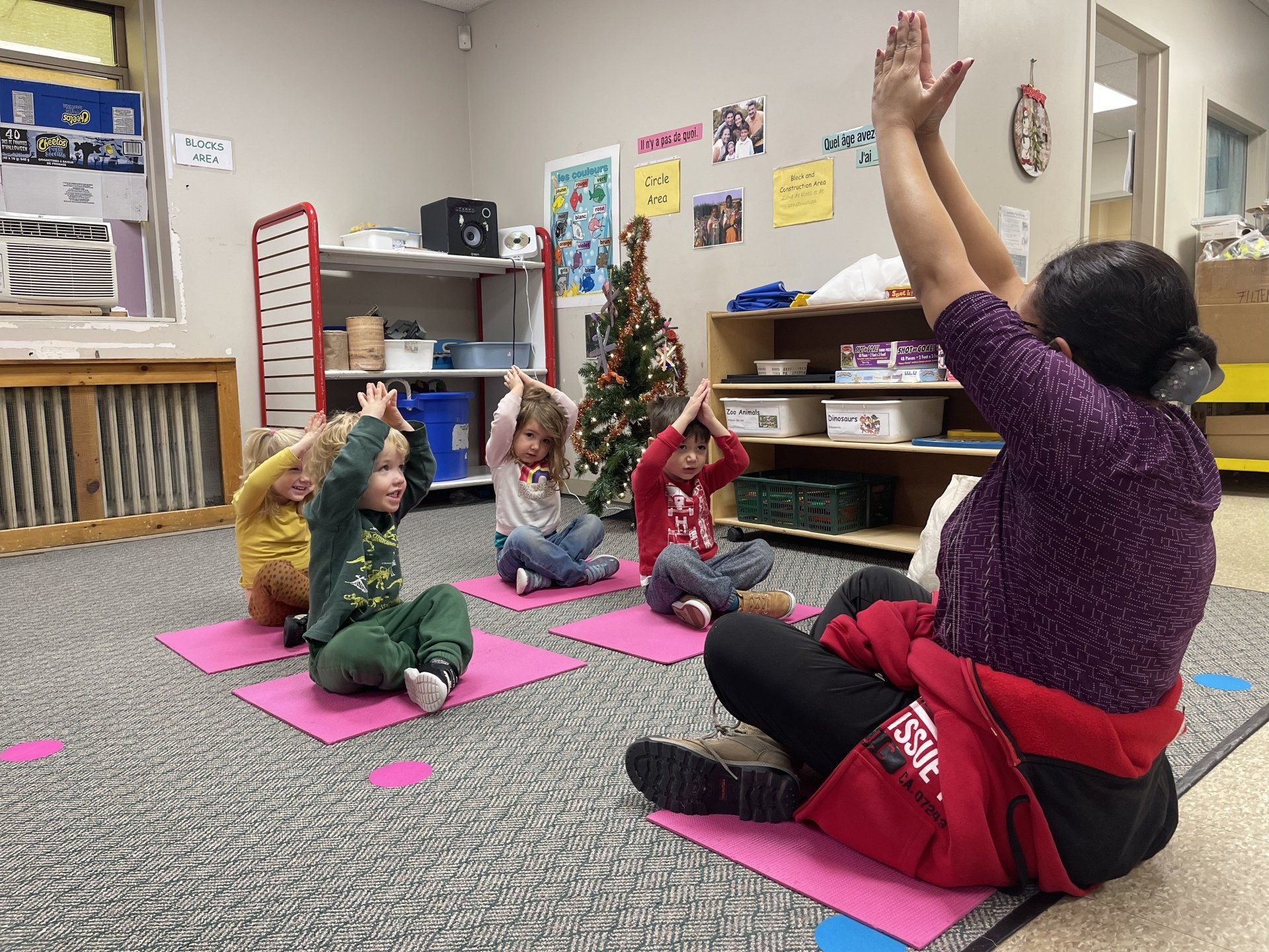 Children doing yoga with an instructor on mats in a classroom.