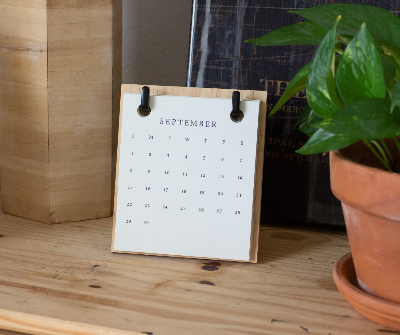 A small calendar is sitting on a wooden table next to a potted plant