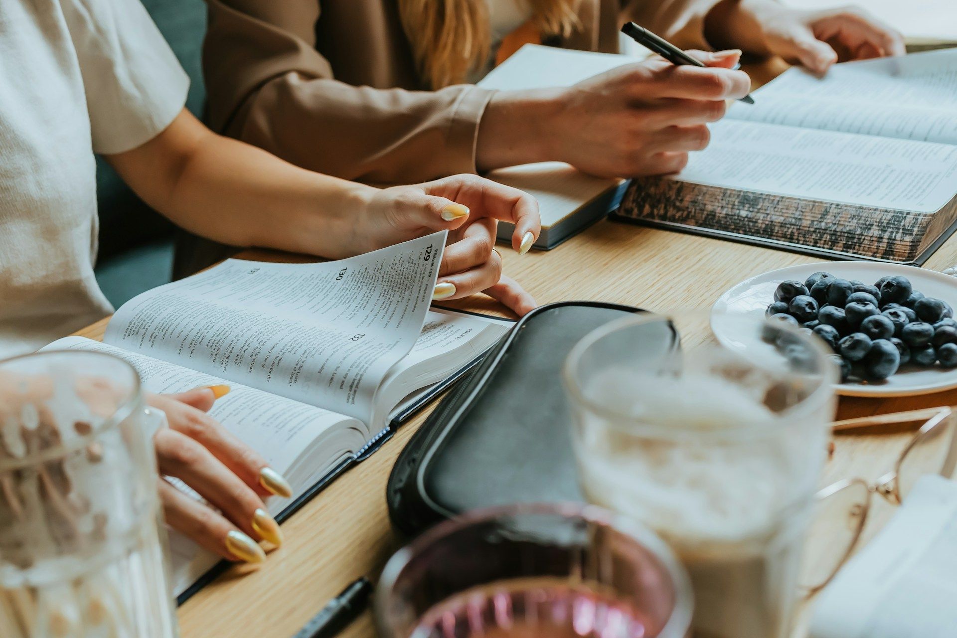 A group of people are sitting at a table reading books and writing in notebooks.