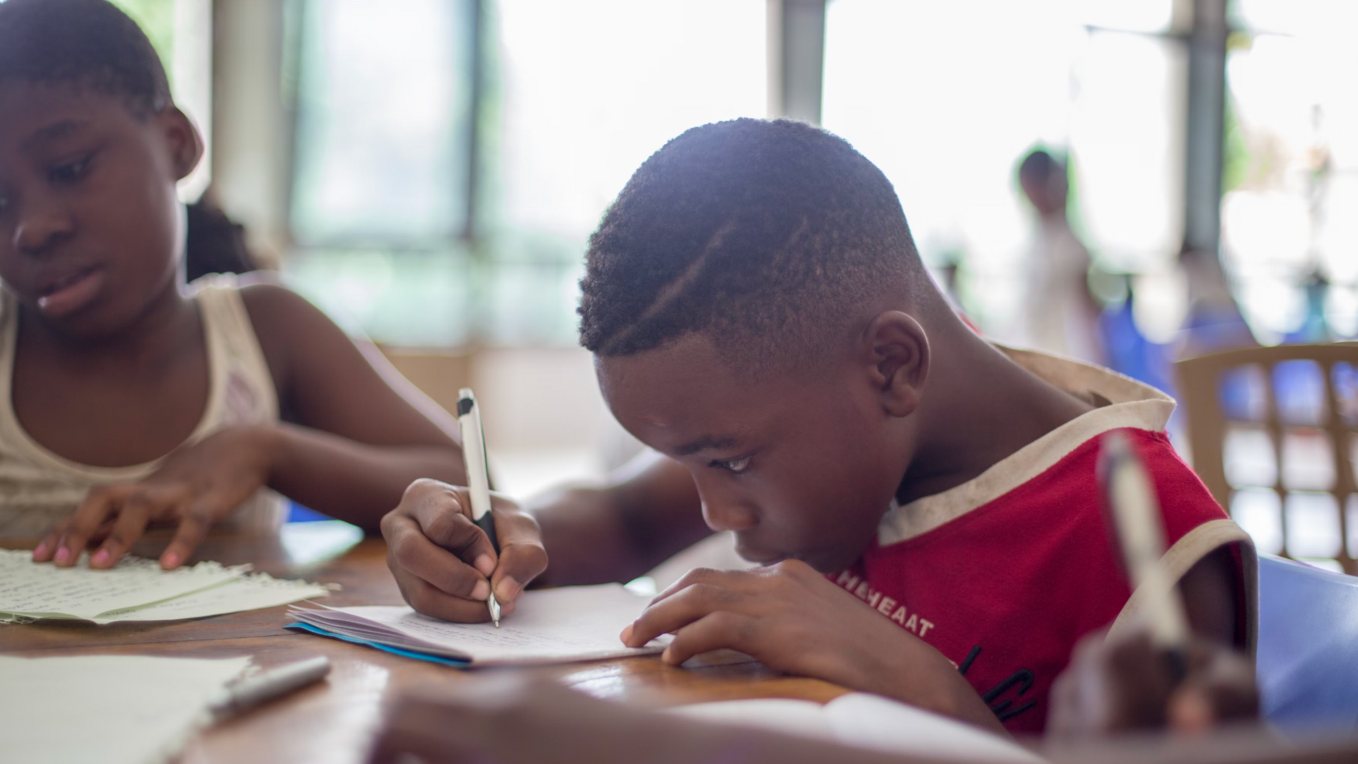 A boy and a girl are sitting at a table writing on a piece of paper.