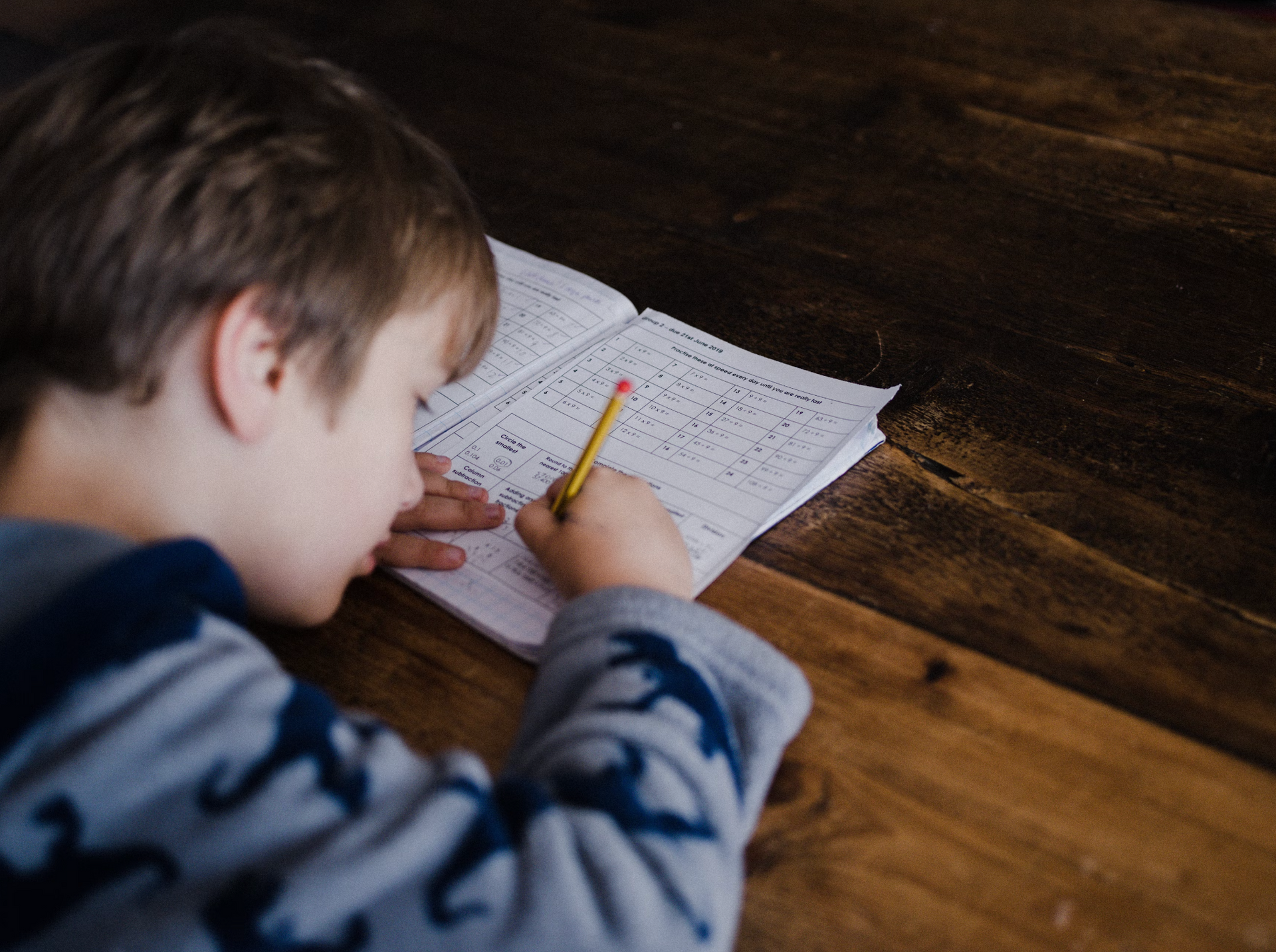 A young boy is sitting at a table writing in a notebook with a pencil.