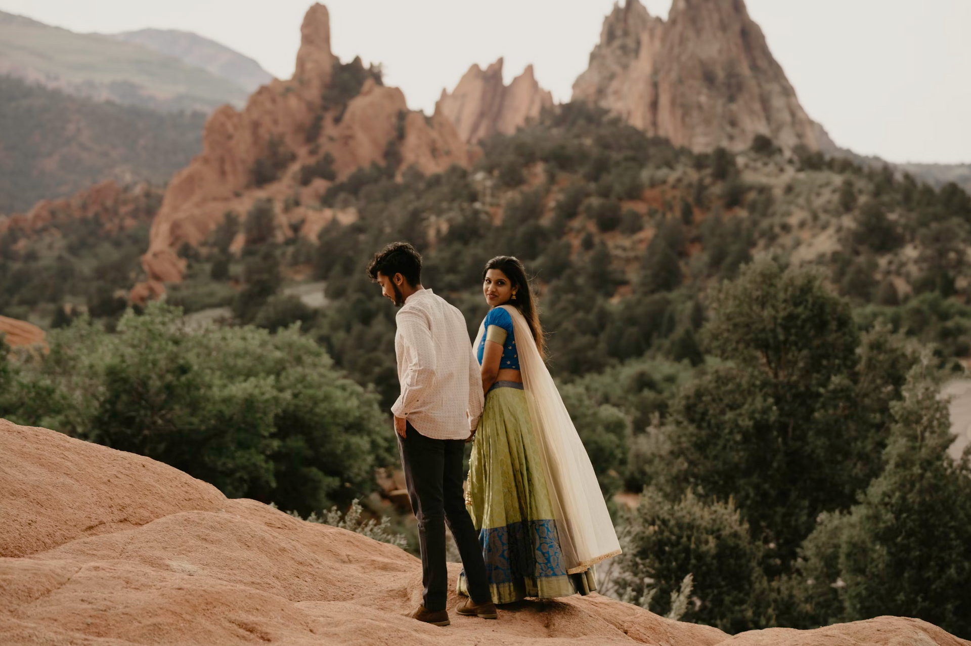 A man and a woman are standing on top of a rocky hill.