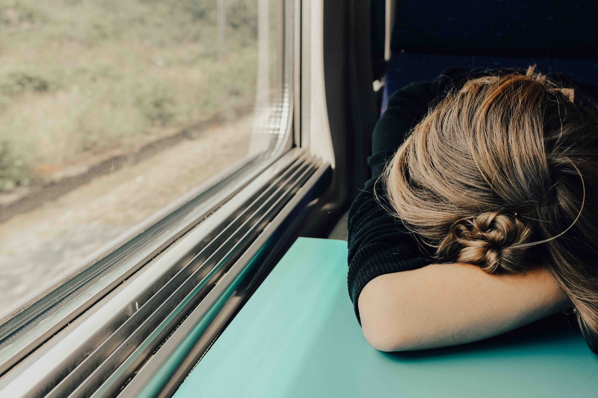 A woman is sleeping on a train with her head on the window sill.