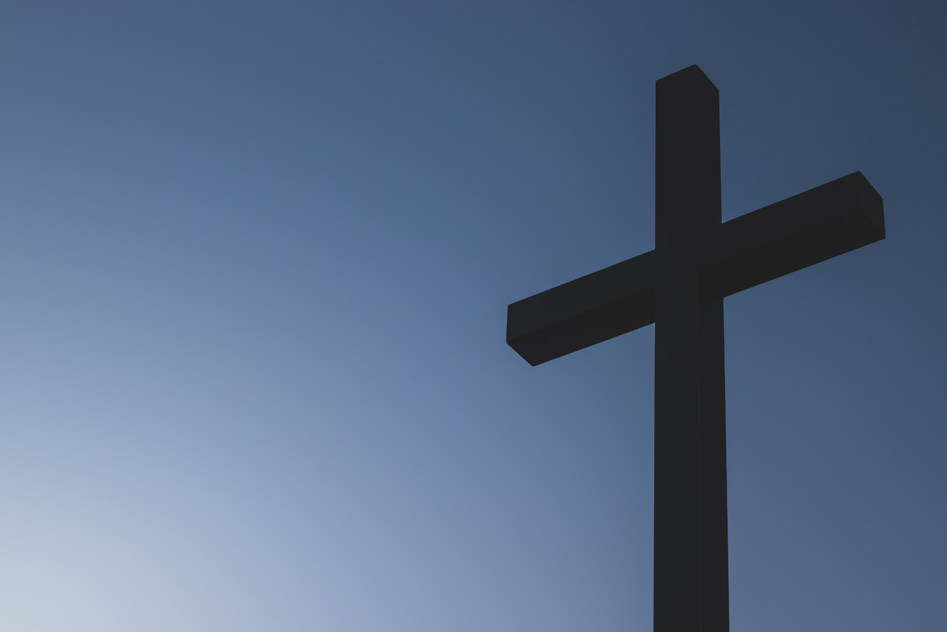 A black cross is silhouetted against a blue sky.