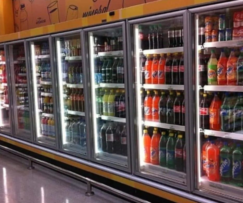Vitrinas de bebidas refrigeradas en una tienda, llenas de varias botellas de refrescos de colores.