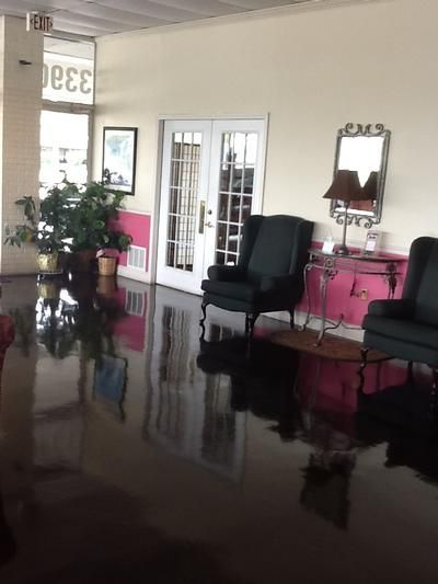 Bright lobby with pink walls, black chairs, a mirror, glass doors, and a polished reflective floor