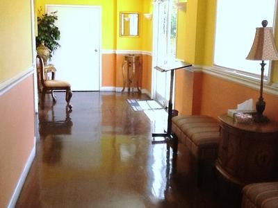 Bright hallway with yellow walls, polished floor, chairs, lamps, and a small table near a white door.