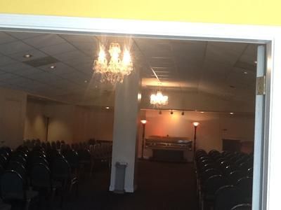 Dim banquet hall with rows of chairs and chandeliers, viewed through a doorway.