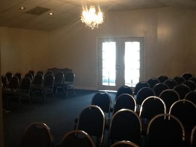 Empty conference room with rows of chairs and a chandelier near tall windows.