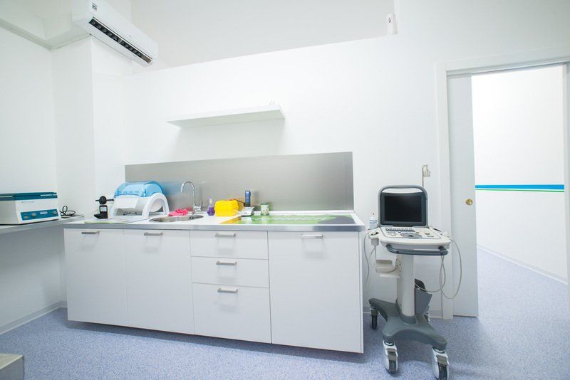Sala visita medica pulita e luminosa, con armadietti bianchi, attrezzature e una porta parzialmente aperta.