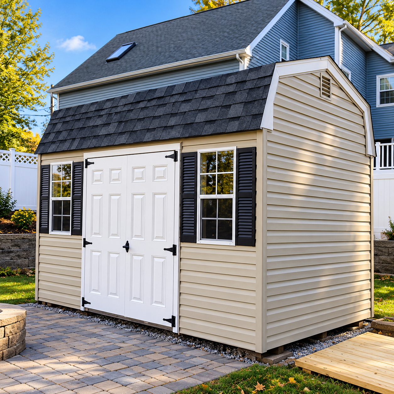 Small beige garden shed with white double doors and dark shingled roof on a paved backyard patio