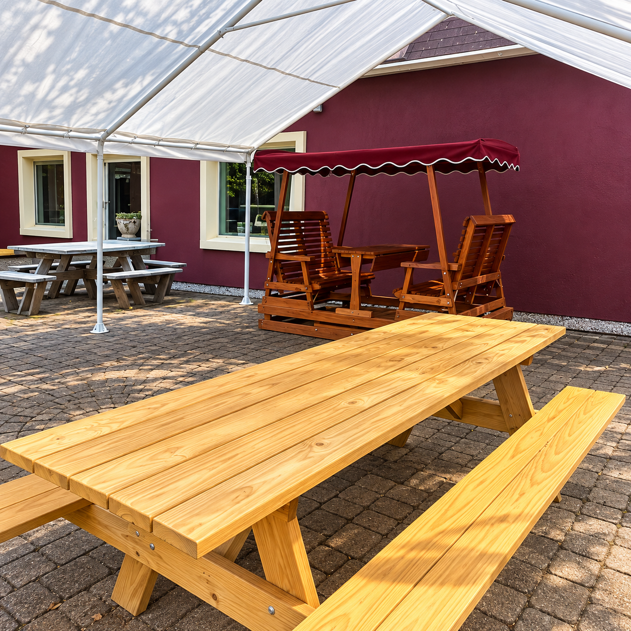 Outdoor seating area with wooden picnic tables beside a purple building and red swing bench under a canopy