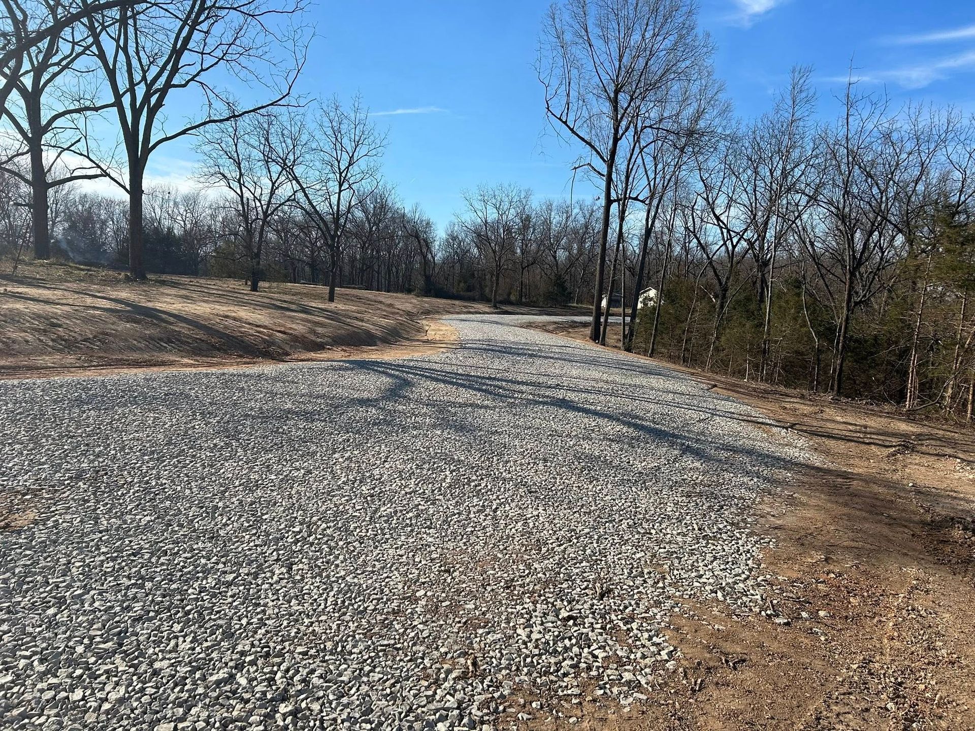 A winding gravel path stretches through a wooded area under a clear blue sky on a sunny day.