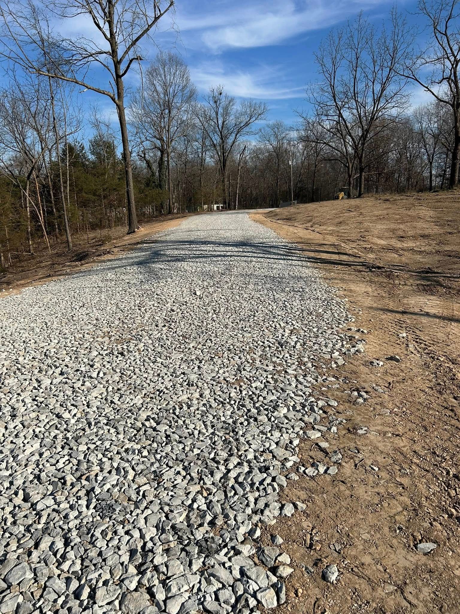 A gravel path leads through a wooded area under a blue sky.
