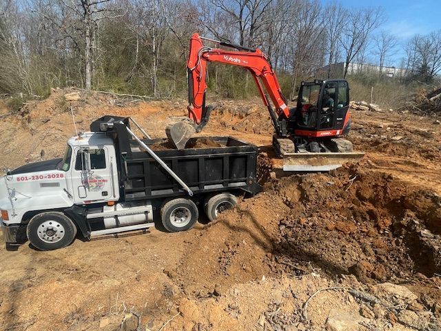 An orange excavator loads dirt into the bed of a white dump truck at an outdoor construction site.