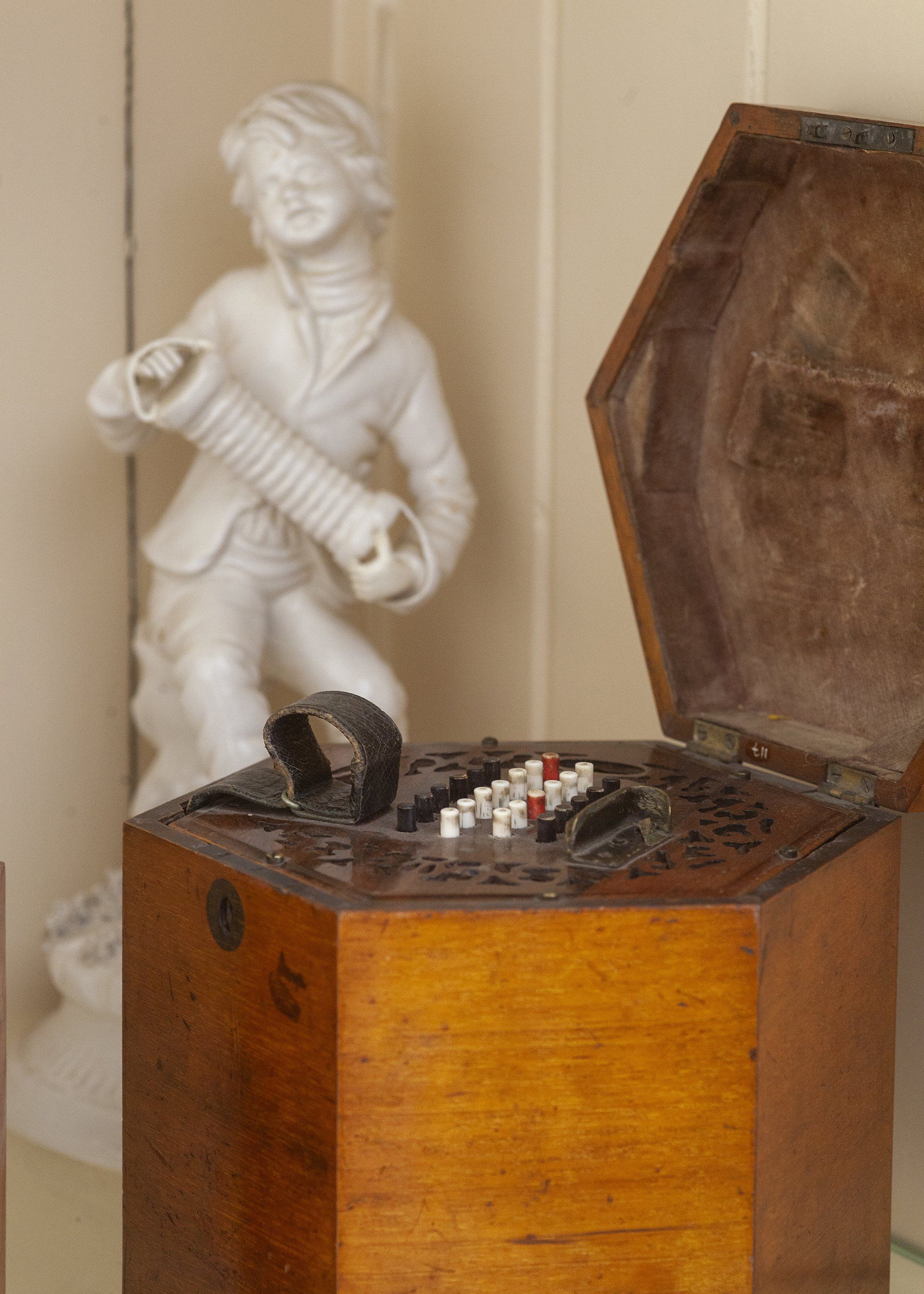 Een beeld van een man die accordeon speelt naast een houten kist