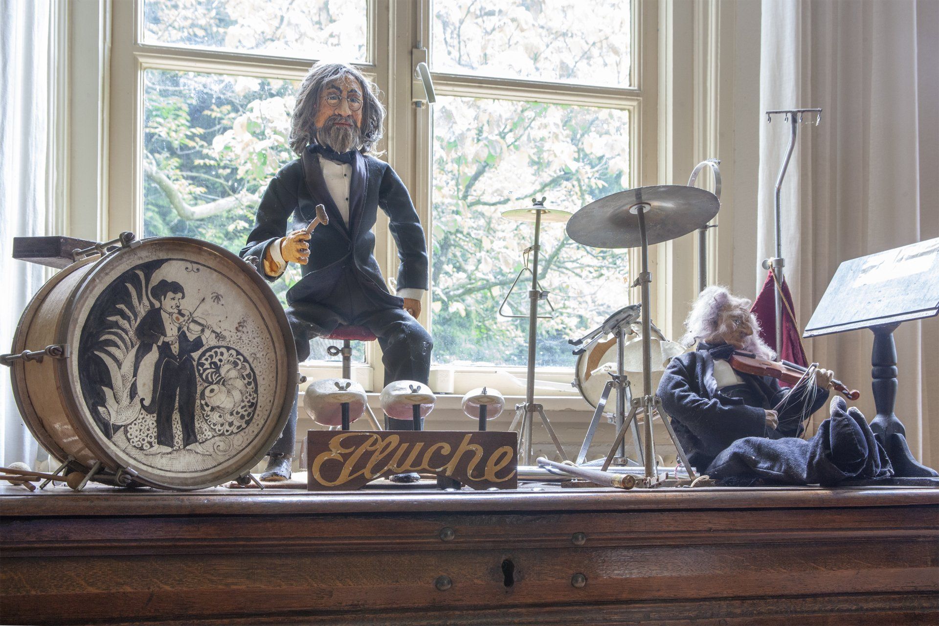 Een trommel en een viool staan ​​op een tafel voor een raam.