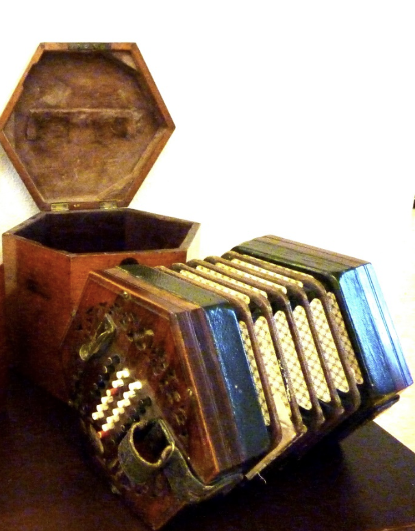 Een antieke concertina met een open, zeshoekige houten behuizing op een donkere ondergrond.