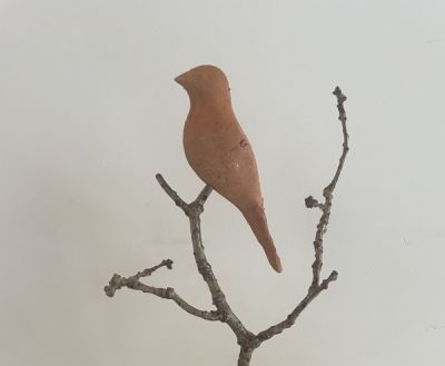 A terracotta bird sculpture perched on a branch affixed to a wooden base.