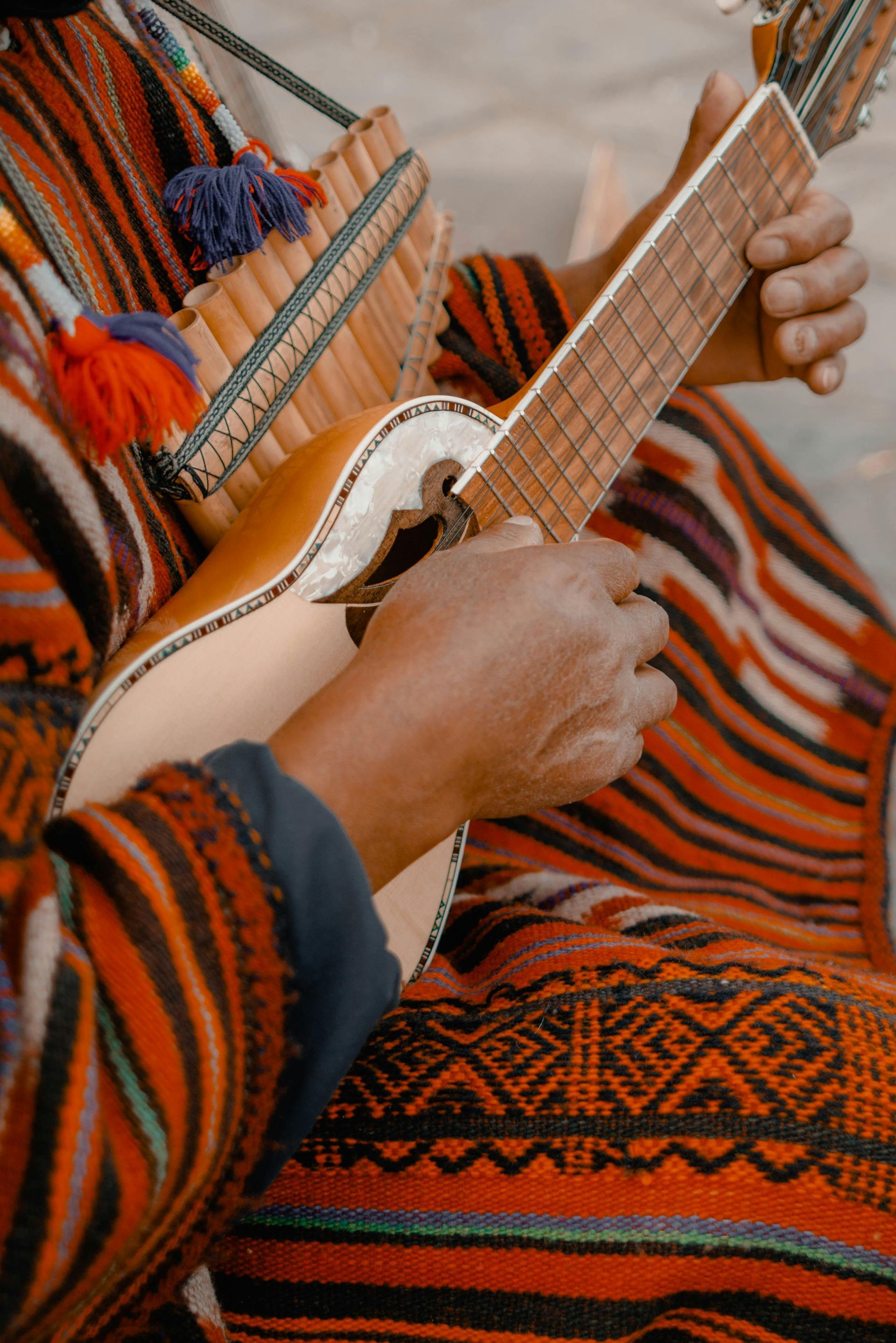 Een persoon bespeelt een charango, een klein snaarinstrument, met zichtbare panfluiten. Op de achtergrond is een kleurrijk geweven textiel te zien.