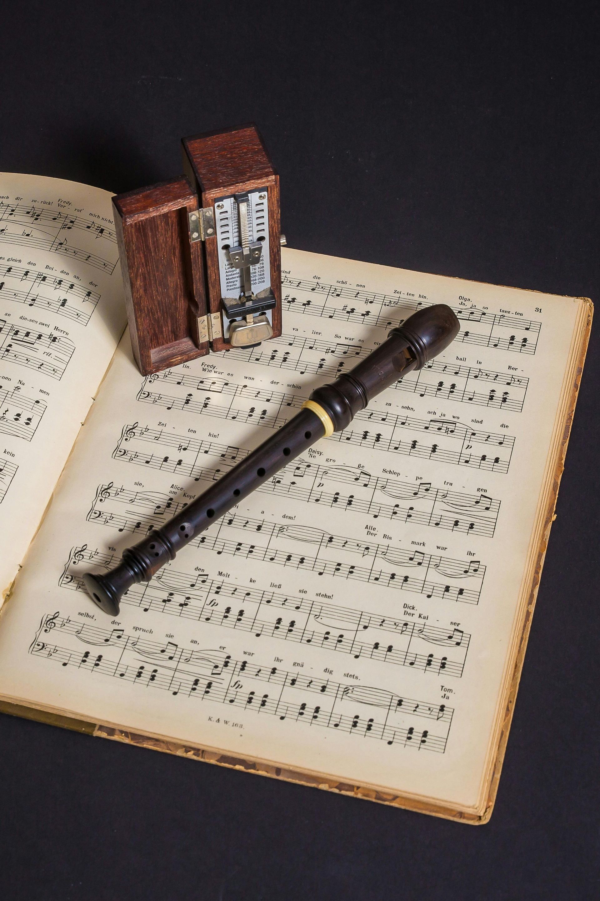 Houten blokfluit en open bladmuziek met een klein bruin klokje op een zwarte achtergrond.