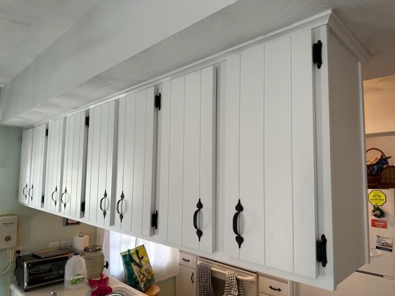 A kitchen with white cabinets and black handles.