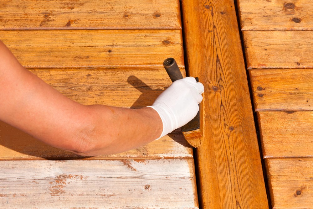 A person is painting a wooden deck with a hammer.