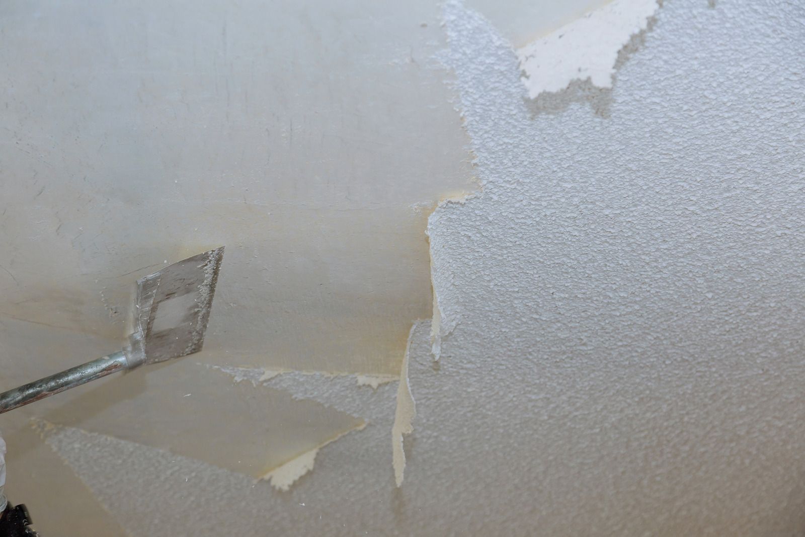 A person is peeling wallpaper from a wall with a spatula.
