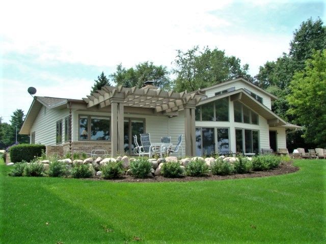 Single-story house with a pergola, large windows, and a lush green lawn under a blue sky