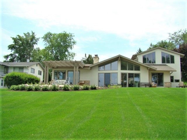 Suburban house with a large green lawn, trees, and a bright blue sky