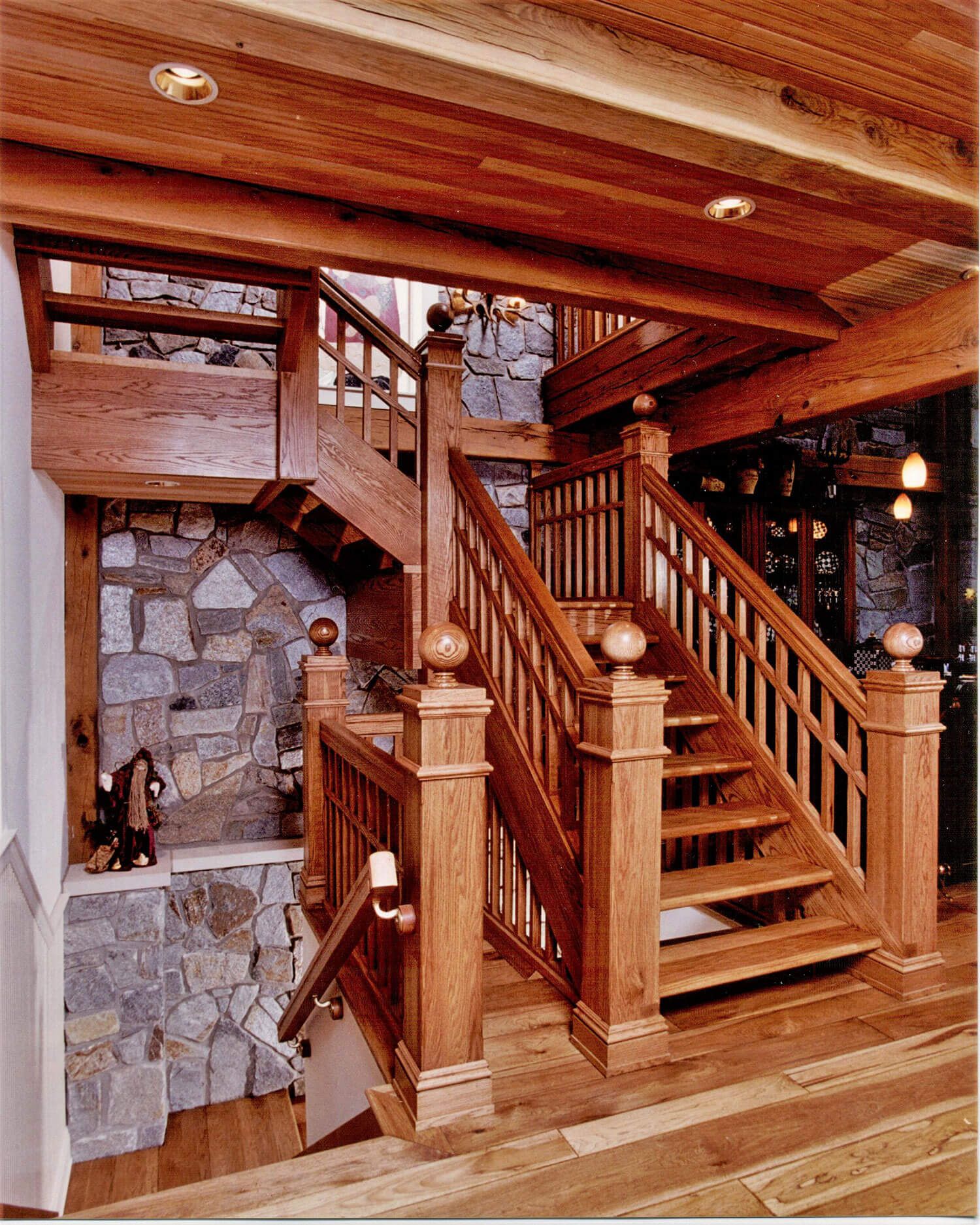 Wood-paneled foyer with a central staircase, stone fireplace, and warm rustic interior lighting