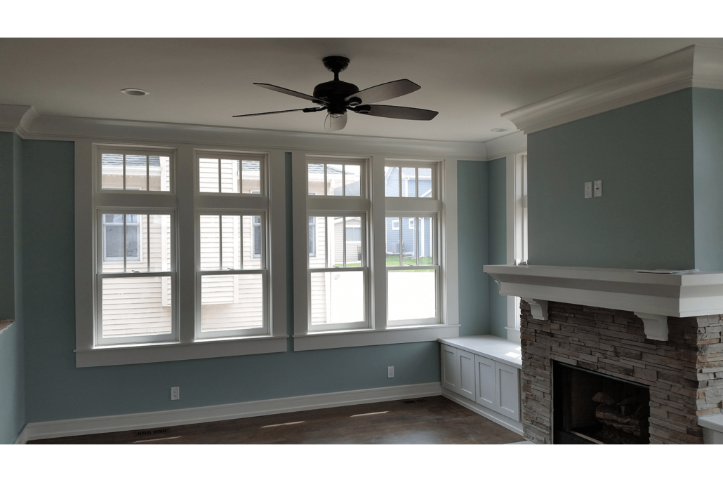 Empty living room with blue walls, large windows, ceiling fan, and a brick fireplace