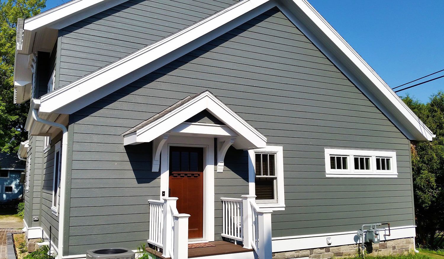 Gray house with white trim, small front porch, and a steep gabled roof on a sunny day