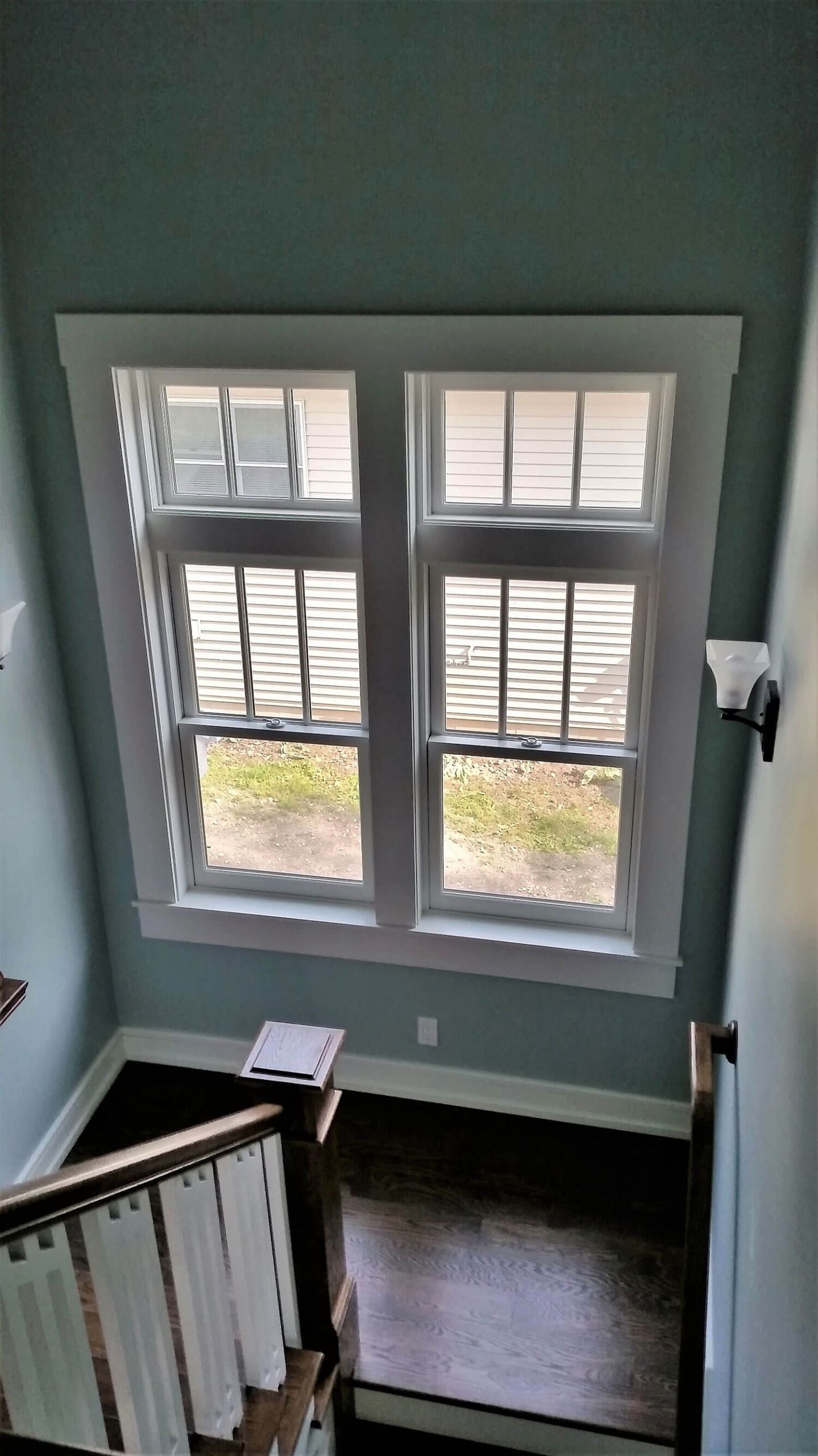 Stairwell with green walls, dark wood floor, and a large window letting in daylight.