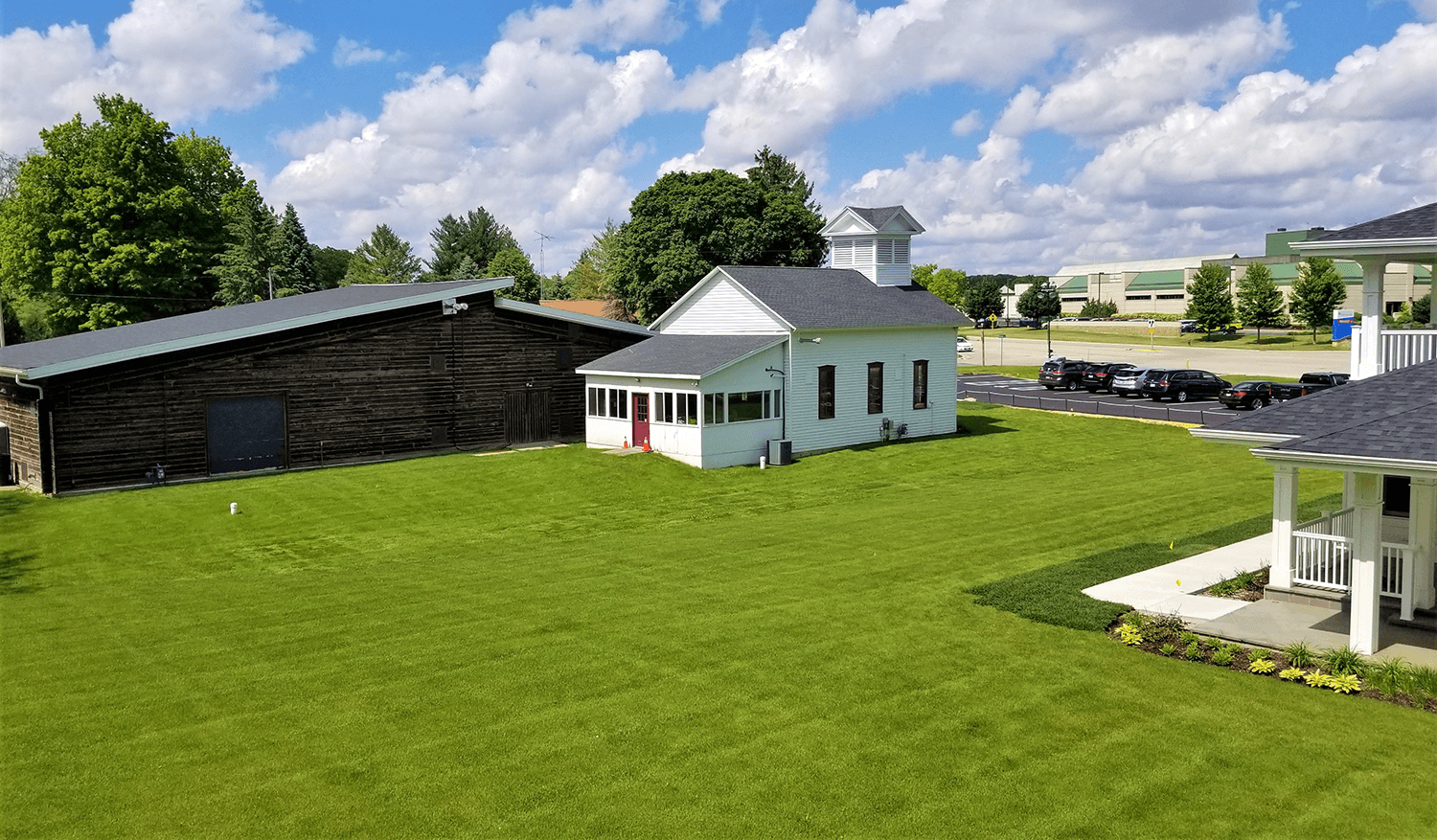 Rural farmyard with a white barn, green lawn, small house, and cloudy sky