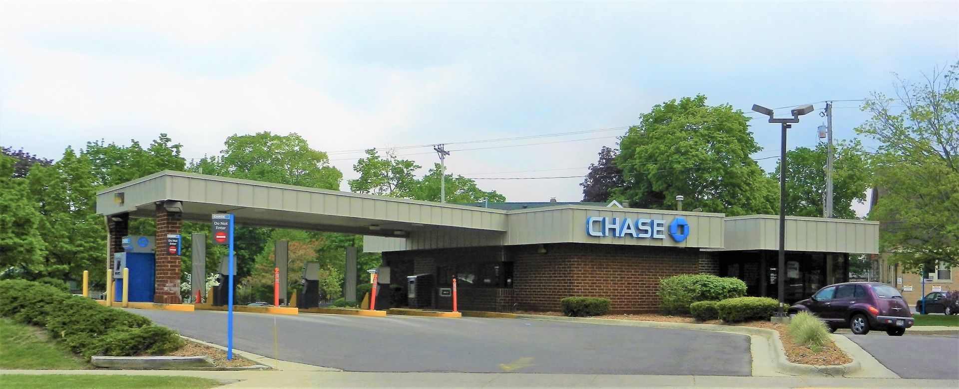 Chase bank branch with drive-through lanes, brick facade, and parked cars on a tree-lined street