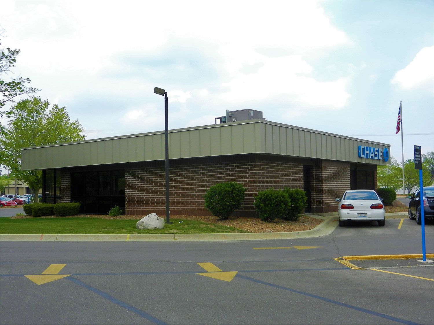 Low, circular brick bank building with green roof, parking lot, and a parked silver car under a cloudy sky